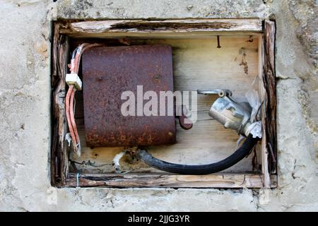 Open wooden electrical power box made from cracked wooden frame filled with rusted metal antique switch and old electrical wires with broken red Stock Photo