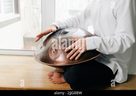 Man playing on hang drum, or Steel Drum, Hangpan, modern steel music instrument at home. Meditation music for relax. Close-up Stock Photo