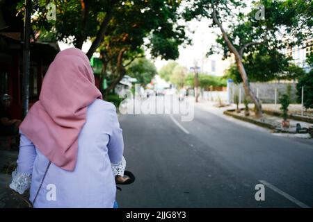 Rear view young asian muslim woman cycling in the street Stock Photo