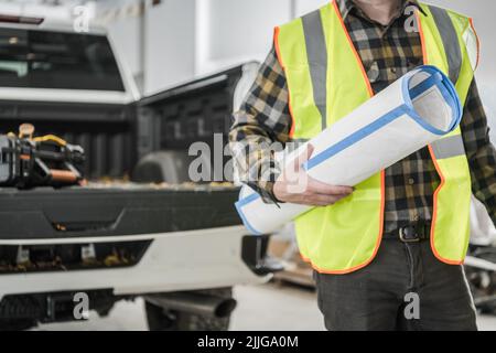 Closeup of Caucasian Supervisor Wearing Yellow Warning Safety Waistcoat with Blueprint Building Plan in His Hands. Construction Site in the Background Stock Photo