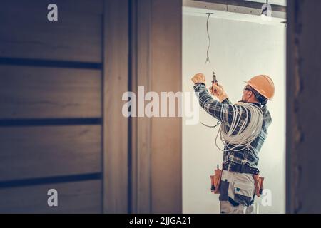 Fully Equipped Professional Electrician Working on Illumination Installation Cutting Cables Using His Wire Cutter. Residential House Renovation Work T Stock Photo