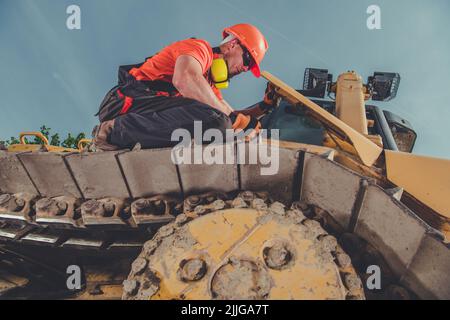 Caucasian Male Construction Worker Sitting on the Top of Continuous Track of His Heavy Duty Machine Checking Its Condition Before Starting the Work. I Stock Photo