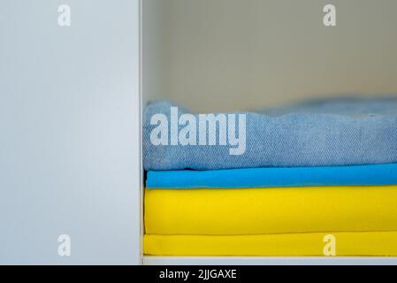 clothes of bright colors are neatly stacked. yellow blue colors of the Ukrainian flag in the closet. Stock Photo