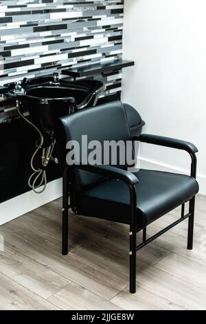 A vertical shot of a black leather chair near a hair washing sink in a salon Stock Photo