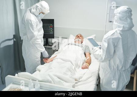 Two unrecognizable doctors wearing protective clothes working with patient suffering coronavirus Stock Photo