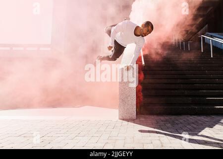 Young man practicing parkour and free running with a smoke grenade. Young male athlete practicing parkour in an urban space. Stock Photo
