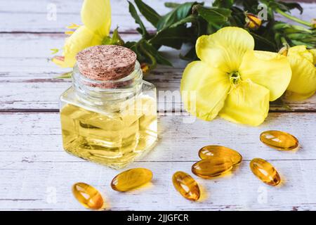 Evening primrose oil in bottle, softgels and flowers on wooden table Stock Photo