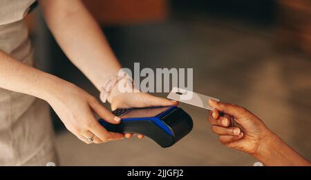 Unrecognizable customer scanning her credit card on a card machine to pay her bill in a cafe. Woman doing a cashless and contactless transaction using Stock Photo