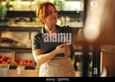 Grocery store owner taking inventory using a digital tablet in her shop. Young female entrepreneur running her small business using wireless technolog Stock Photo