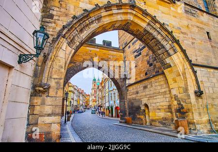 The stone arches of Mala Strana Bridge Tower of Charles Bridge with a view of the colored housing and dome of St Nicholas Church in background, Prague Stock Photo