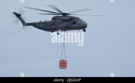 Falkenberg, Germany. 26th July, 2022. A Bundeswehr helicopter flies over the Elbe-Elster forest fire region with a water tank. Credit: Sebastian Willnow/dpa/Alamy Live News Stock Photo