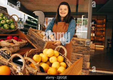 Happy woman with Down syndrome smiling while standing in the vegetable section of a grocery store. Empowered woman with an intellectual disability wor Stock Photo