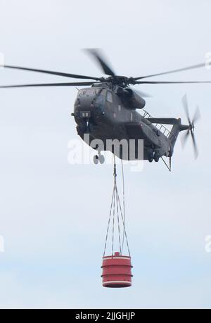 Falkenberg, Germany. 26th July, 2022. A Bundeswehr helicopter flies over the Elbe-Elster forest fire region with a water tank. Credit: Sebastian Willnow/dpa/Alamy Live News Stock Photo