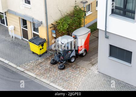 Top above view of small sweeping vacuum cleaner machine equipment removing dust rubbish city street sidewalk paved road near apartment condo building Stock Photo