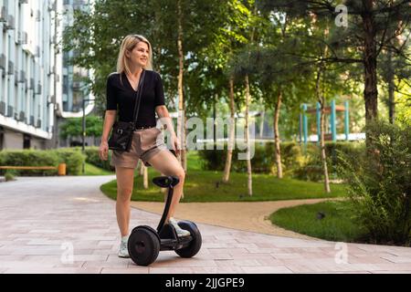 Back view of active tourist woman standing on electric self-balancing scooter at sunny park., young hipster girl driving on modern hover-board at Stock Photo