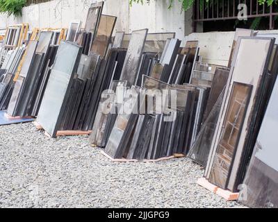 Installation of modern windows in new houses. A lot of double-glazed windows are standing in the yard near the concrete fence. Stock Photo