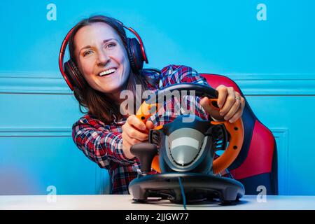 Gamer woman in headphones playing race game with steering wheel Stock Photo