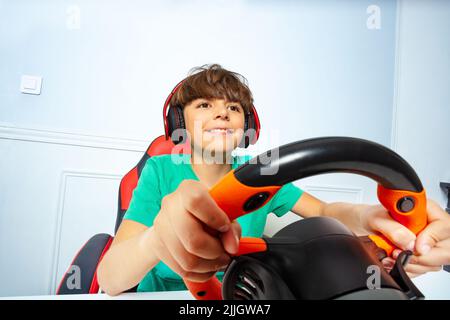 Cute boy in headphones with steering wheel play race game Stock Photo