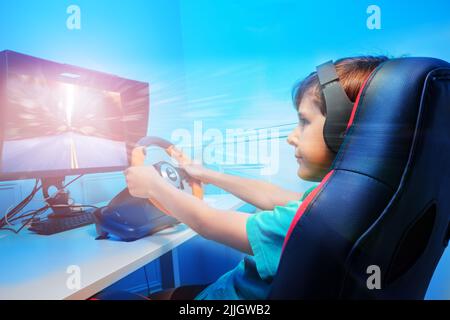 Boy with hands on steering wheel in headphones playing race game Stock Photo