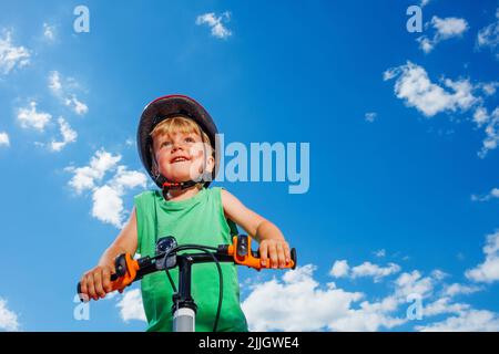 Low angle portrait of a little smiling boy ride small bicycle Stock Photo