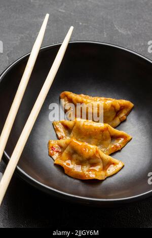 Chopsticks and three gyoza dumplings in black bowl. Close-up. Black background Stock Photo