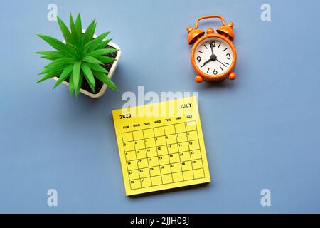 July 2023 calendar on adhesive note with alarm clock set at 8 o'clock. Stock Photo