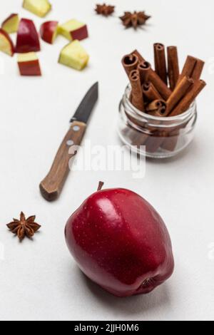 Ripe red apple on table. Cinnamon sticks in glass jar. Chopped apples and knife on table. Top view. White background Stock Photo