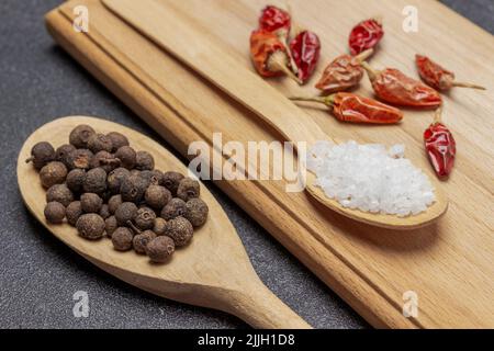 Allspice in wooden spoon. Pods of red pepper and salt blackboard. Close up. Black background Stock Photo