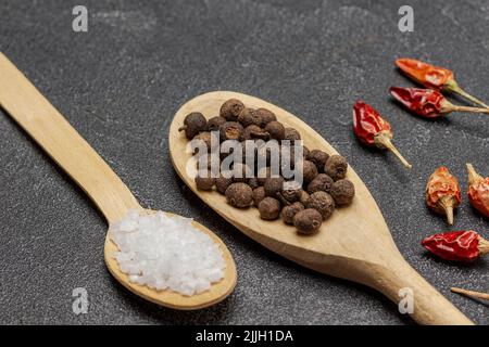 Salt and allspice in wooden spoons. Pods of red pepper on the table. Close up. Top view. Black background Stock Photo