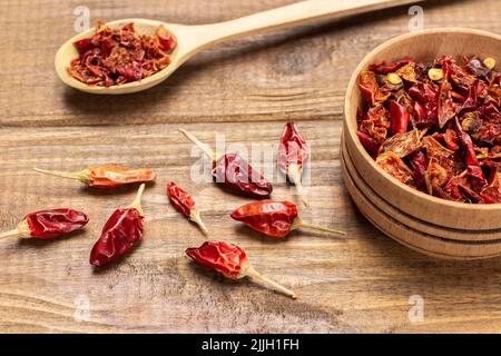 Pods of dry red pepper in wooden bowl and on table. Top view. Wooden background Stock Photo