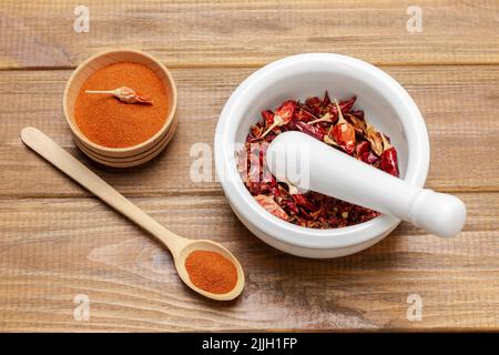 Dry red pepper pods in porcelain mortar. Ground red pepper in wooden bowl. Flat lay. Wooden background Stock Photo