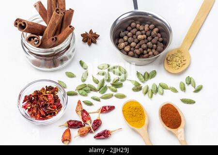 Allspice in metal bowl and cinnamon sticks in jar. Ground spices paprika, turmeric and ginger. Cardamom seeds and dry red pepper pods. Top view. White Stock Photo