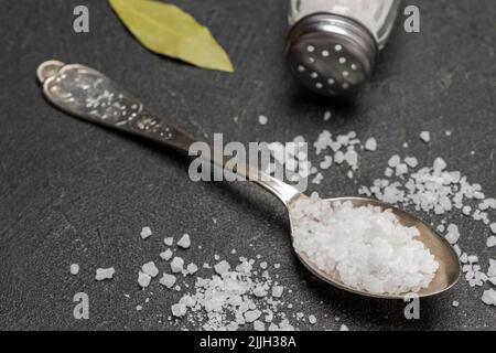 Salt in metal spoon. Salt shaker and bay leaf. Close up. Black background Stock Photo