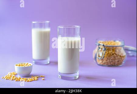 Vegan healthy pea milk in two glasses, pea seeds. Lilac background. Copy space Stock Photo