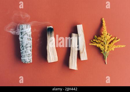 Items for spiritual cleansing - sage and various herbs bundles, palo santo  incense sticks and candle on green background with shadows. Stock Photo