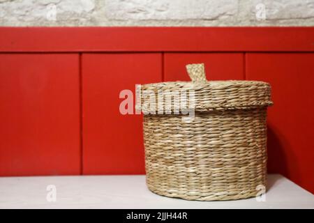 a round wicker container with a lid on a red wall background.  Stock Photo