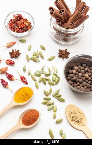 Allspice in metal bowl and cinnamon sticks in jar. Ground paprika, turmeric and ginger spices in wooden spoons. Cardamom seeds and dry pepper pods on Stock Photo