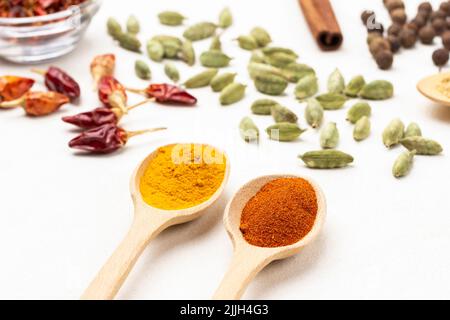 Ground paprika and turmeric spices in wooden spoons. Cardamom seeds and dry pepper pods on table. Top view. White background Stock Photo