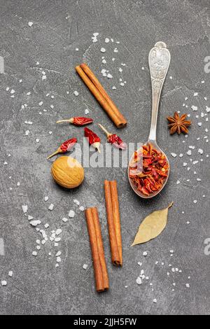 Dry peppers in metal spoon, pepper pods and cinnamon sticks on table. Copy space. Flat lay. Black background Stock Photo