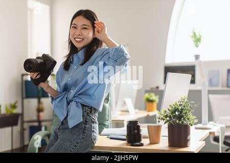 Young Korean Female Photographer Holding Photocamera Standing At Home Stock Photo