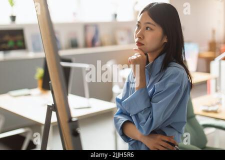 Thoughtful Asian Businesswoman Looking At Whiteboard In Modern Office Stock Photo