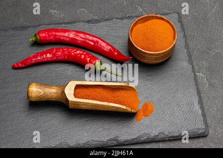 Pods of fresh red pepper and ground paprika in scoop and in bowl on stone board. Top view. Black background Stock Photo