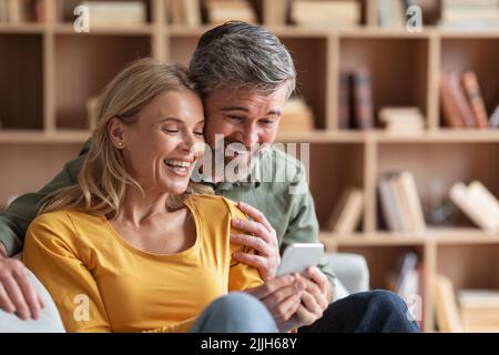 Happy Middle Aged Couple Watching Family Photos On Smartphone At Home Stock Photo