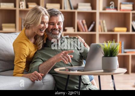 Digital Entertainment. Cheerful Middle Aged Couple Using Laptop At Home Together Stock Photo