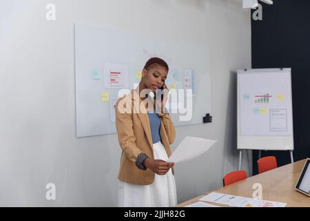 African american young businesswoman talking on smart phone and analyzing document in office Stock Photo