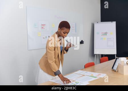 African american young businesswoman talking through smart phone and analyzing charts in office Stock Photo