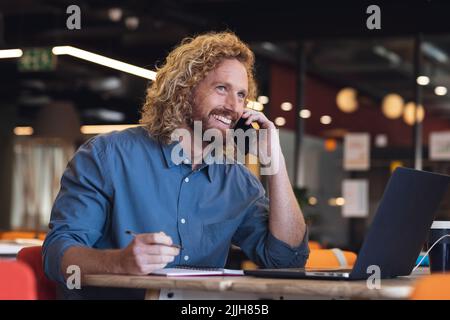 Cheerful young caucasian businessman looking away while talking on smart phone in creative office Stock Photo