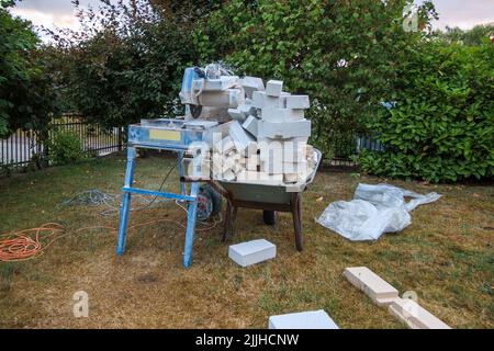 Next to a circular saw for stones there is a wheelbarrow with stone scraps Stock Photo