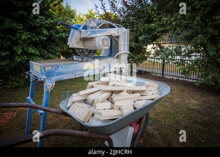 Next to a circular saw for stones there is a wheelbarrow with stone scraps Stock Photo