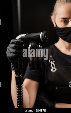 The master of instant tanning holds a spray pen with lotion. Express tan in a beauty salon. Stock Photo